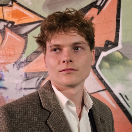 Dylan Thomas in a tweed jacket, standing in front of a painted mural.